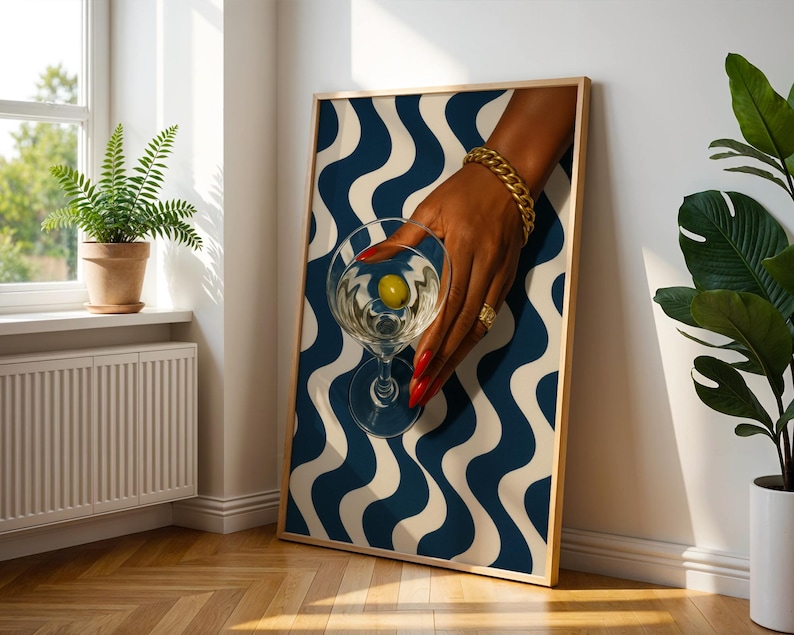 Peut inclure: Impression d'art encadr&eacute;e repr&eacute;sentant une main tenant un verre &agrave; martini avec une olive. La main est orn&eacute;e de bijoux dor&eacute;s et de vernis &agrave; ongles rouge. Le fond pr&eacute;sente un motif ondul&eacute; bleu et blanc.