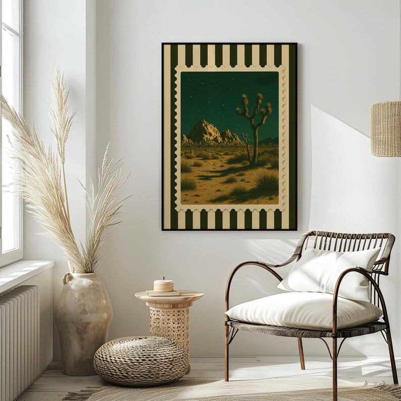 May include: A framed art print depicting a desert landscape with a Joshua tree under a starry night sky. The artwork is framed with a black border and a decorative stamp-like edge. The print hangs on a white wall above a woven chair.