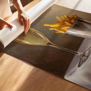May include: A still-life painting depicts a champagne glass and a metal cup filled with french fries. The glass is filled with a bubbly liquid. The fries are golden brown. The painting is on a surface, with a roll of paper being unrolled.