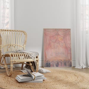 May include: A light brown wicker chair with a woven seat and a throw blanket draped over the back. The chair is sitting on a light brown oval rug in a room with white walls and white curtains. A framed painting of a pink stage curtain with people in the background hangs on the wall.