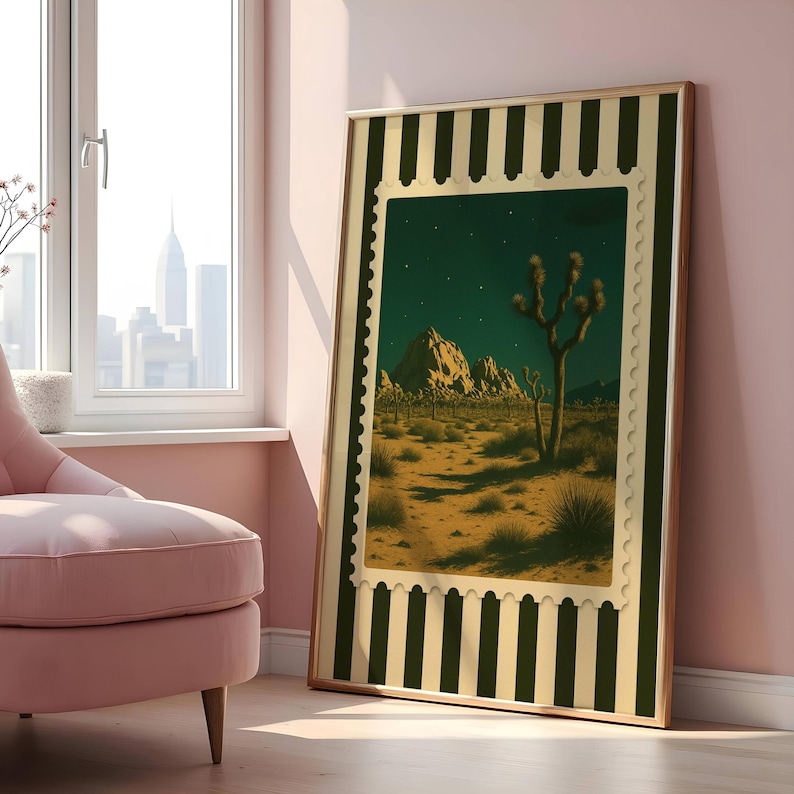 May include: A framed art print featuring a desert landscape with Joshua trees under a starry night sky. The artwork is framed with a green and cream striped border and a gold-colored frame. The print is leaning against a pink wall.