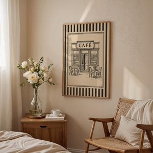 May include: A framed black and white print of a cafe with the word "CAFE" above the entrance. The print is in a room with a wooden nightstand, a vase of flowers, and a wooden chair.