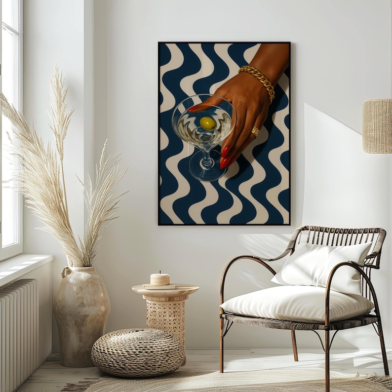 Peut inclure: Impression encadr&eacute;e d'un verre &agrave; martini avec une olive, tenu par une main avec du vernis &agrave; ongles rouge et des bijoux dor&eacute;s. Le fond pr&eacute;sente un motif ondul&eacute; bleu et cr&egrave;me. L'impression est expos&eacute;e dans une pi&egrave;ce avec une chaise et un vase d&eacute;coratif.