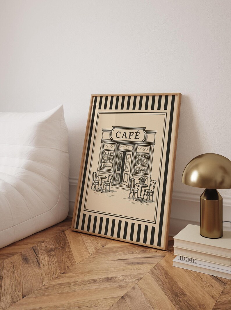May include: Framed art print featuring a black and white illustration of a cafe with outdoor seating. The word "CAF&Eacute;" is displayed above the entrance. The print has a beige background with a black and white striped border and a wooden frame.