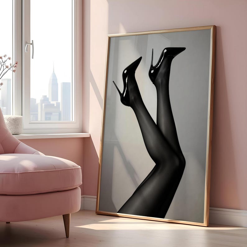May include: A framed art print featuring a pair of legs in black sheer stockings and high-heeled black pumps. The artwork is displayed in a room with a pink wall and a window overlooking a cityscape.