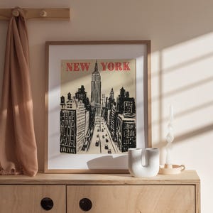 May include: A framed print of a black and white illustration of the New York City skyline with the Empire State Building in the center. The text "NEW YORK" is in red letters at the top of the print.