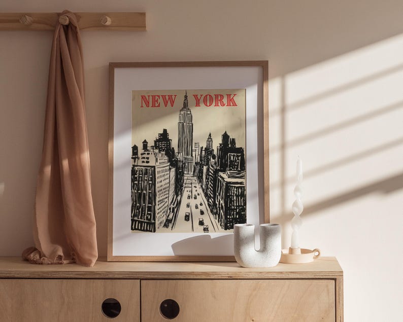 May include: A framed print of a black and white illustration of the New York City skyline with the Empire State Building in the center. The text "NEW YORK" is in red letters at the top of the print.