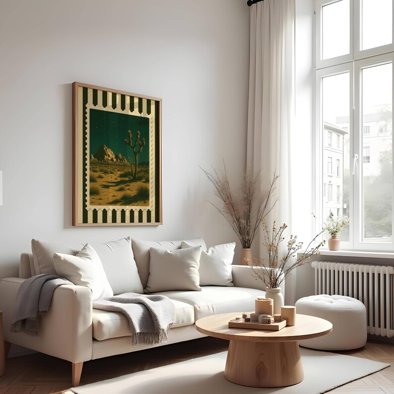 May include: A framed desert landscape art print featuring a Joshua tree under a starry night sky. The artwork has a gold and black border and is displayed above a white sofa in a living room setting. The room is decorated with neutral tones.