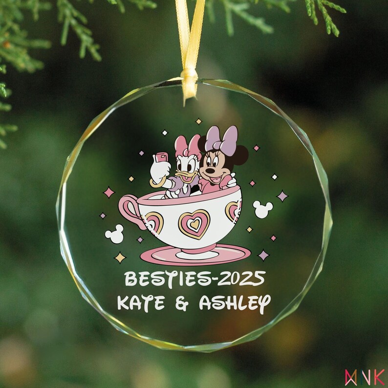 Besties ornament 2025 printed on a clear glass ornament with a Minnie and Daisy inspired teacup design and custom friend names.