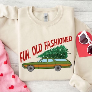 May include: Cream-colored sweatshirt with the words "FUN, OLD FASHIONED" in red. A green and orange station wagon carries a Christmas tree on top. White heart-shaped sunglasses and a red heart are visible.