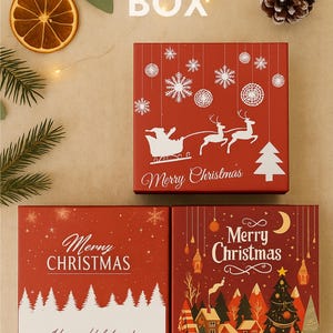 Three red Christmas-themed gift boxes with festive prints displayed on a beige background. Surrounding details include pinecones, orange slices, and fairy lights, highlighting the “Free Gift Box” offer for ornaments.