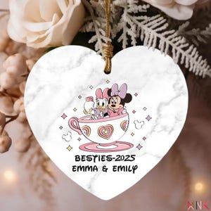 Besties ornament 2025 on a heart-shaped ceramic ornament featuring a cute Minnie and Daisy style teacup illustration with custom names.