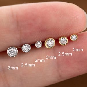 Puede incluir: Colección de seis pendientes de botón con gemas redondas y transparentes. Los pendientes varían en tamaño, el más grande mide 3 mm y el más pequeño 2 mm. Algunos tienen engaste plateado, otros dorado.