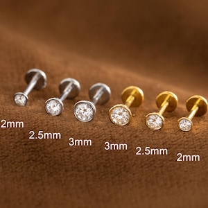 Op de afbeelding: Een verzameling kleine oorstekers met heldere, ronde edelstenen. De oorbellen zijn verkrijgbaar in verschillende maten, waaronder 2 mm, 2,5 mm en 3 mm. Sommige zijn zilverkleurig, andere goudkleurig, allemaal met een platte achterkant.