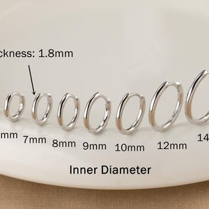 May include: A collection of silver hoop earrings of varying sizes, ranging from 5mm to 14mm inner diameter, displayed on a white surface. The thickness of the earrings is 1.8mm. The text "Inner Diameter" is also visible.