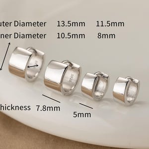 Può includere: Quattro orecchini a cerchio in argento di diverse dimensioni sono esposti su un piatto bianco. I diametri esterni sono di 13,5 mm e 11,5 mm. I diametri interni sono di 10,5 mm e 8 mm. Lo spessore è di 7,8 mm e la larghezza è di 5 mm.