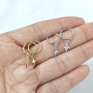 Puede incluir: Dos pares de pendientes de aro, uno dorado y otro plateado, cada uno con un dije de estrella colgante. Los pendientes se muestran sobre un fondo claro, mostrando su dise&ntilde;o delicado. Una joya sencilla y elegante.