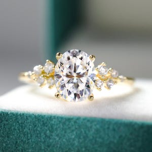 Pode incluir: Um anel de ouro com uma pedra central de diamante oval e diamantes menores engastados em um design de folha na banda.