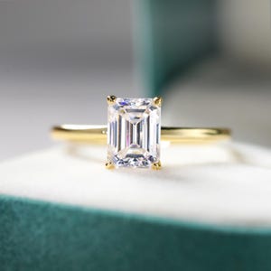 May include: A gold ring featuring a large, clear, square-shaped emerald cut diamond.