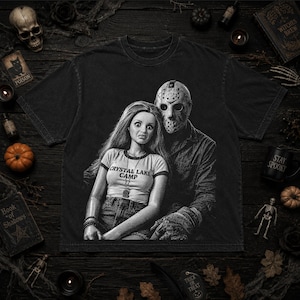 Peut inclure: Un t-shirt noir &agrave; manches courtes avec une impression graphique repr&eacute;sentant une poup&eacute;e aux longs cheveux portant un haut marqu&eacute; CRYSTAL LAKE CAMP, assise &agrave; c&ocirc;t&eacute; d'une silhouette portant un masque de hockey. Le design est monochrome et vieilli.