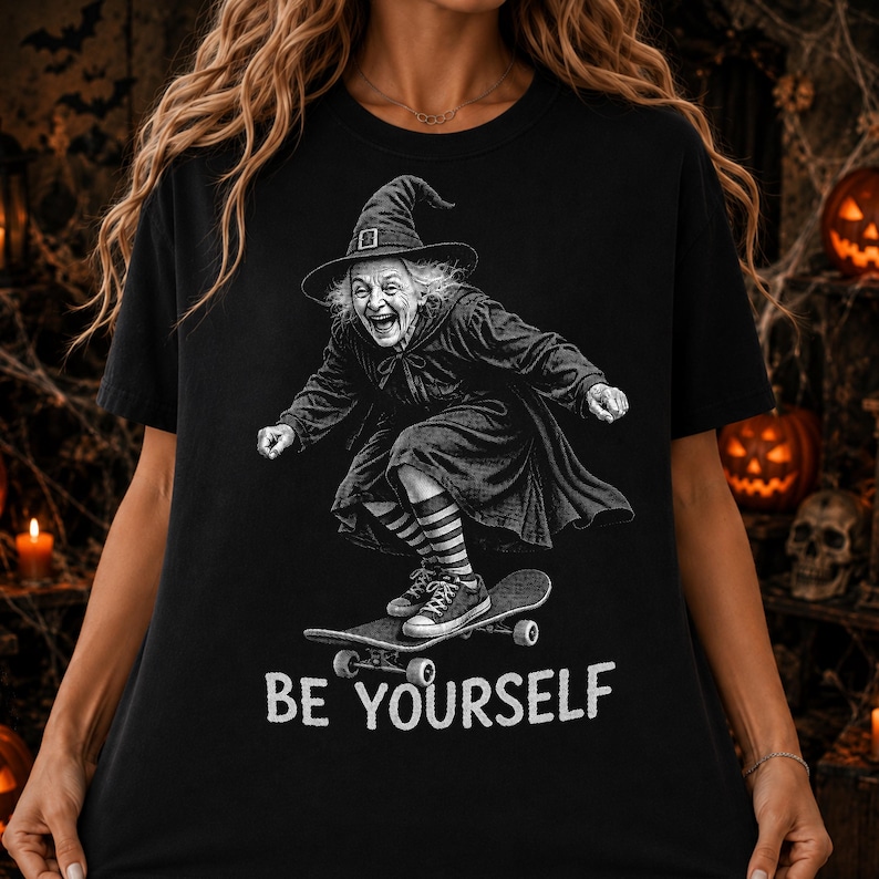 May include: A black t-shirt featuring a white graphic of an elderly person wearing a witch hat and a cloak while riding a skateboard. The person wears striped socks and sneakers. The text "BE YOURSELF" is printed in white below the graphic.