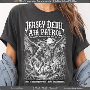 Könnte beinhalten: Ein anthrazitfarbenes T-Shirt mit einem weißen Grafikdruck einer geflügelten Kreatur über einem Wald. Der Text lautet JERSEY DEVIL AIR PATROL, PINE BARRENS NOCTURNAL ENFORCEMENT EST. 1735 und LOST IN THE PINES? WORSE THINGS ARE AIRBORNE.