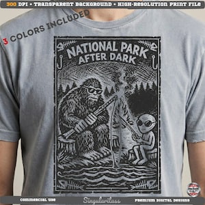 May include: Gray t-shirt featuring a black and white graphic of Bigfoot and an alien fishing by a campfire. The text "NATIONAL PARK AFTER DARK" is above the image. Includes the text "3 COLORS INCLUDED".