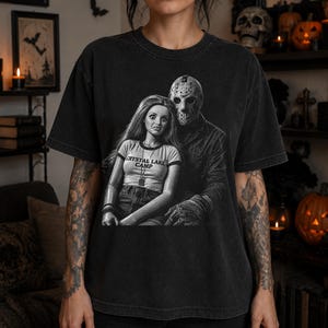 Peut inclure: Un t-shirt noir &agrave; manches courtes avec une impression graphique repr&eacute;sentant une poup&eacute;e aux longs cheveux portant un haut marqu&eacute; CRYSTAL LAKE CAMP, &agrave; c&ocirc;t&eacute; d'une silhouette portant un masque de hockey. Le motif est en noir et blanc.