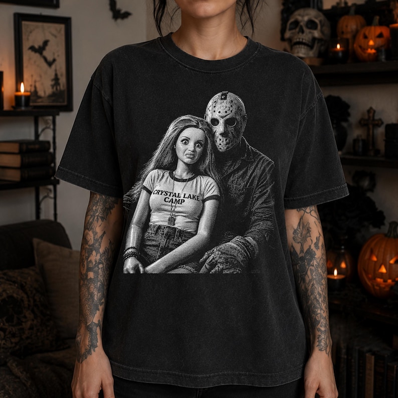 Peut inclure: Un t-shirt noir &agrave; manches courtes avec une impression graphique repr&eacute;sentant une poup&eacute;e aux longs cheveux portant un haut marqu&eacute; CRYSTAL LAKE CAMP, &agrave; c&ocirc;t&eacute; d'une silhouette portant un masque de hockey. Le motif est en noir et blanc.
