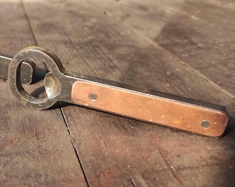 May include: A vintage bottle opener with a metal head and a copper-colored handle. The opener is designed with a circular opening for removing bottle caps. The handle has two small rivets.