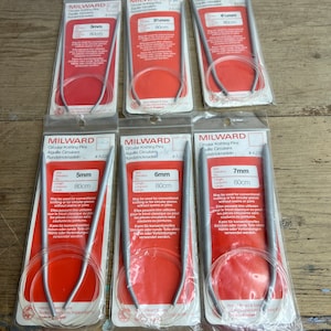 May include: A set of ten silver circular knitting needles in various sizes, packaged in individual plastic bags. Each bag features a red label with the brand name "MILWARD" and the size and length of the needles in both inches and centimeters.