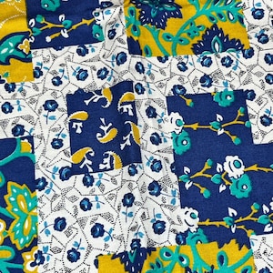 May include: A patchwork fabric with a repeating pattern of blue, yellow and green floral designs. The fabric has a white background with a small, repeating pattern of blue and white dots.