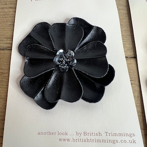 May include: Black fabric flower applique with a sparkly center. The applique is labeled "Furnishing Applique" and "Sew ons" on a white card. The card also says "another look... by British Trimmings www.britishtrimmings.co.uk".