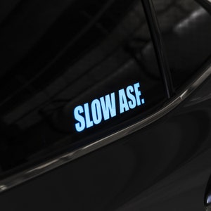 May include: A black car with a blue and white sticker that says "SLOW ASF." on the back window.