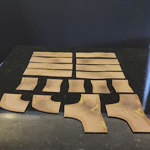 May include: A set of 14 brown and tan cardboard pieces for a tabletop game. The pieces are shaped like paths and curves, and they have a textured surface.