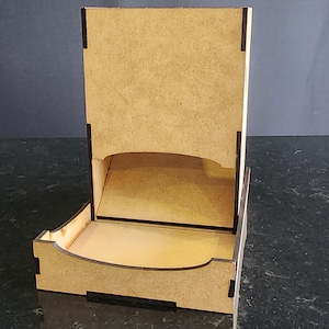 Puede incluir: Expositor de madera marrón claro con respaldo rectangular y estante frontal curvo. El expositor tiene una ranura en la parte trasera y juntas de esquina visibles. Diseñado para exhibir artículos.