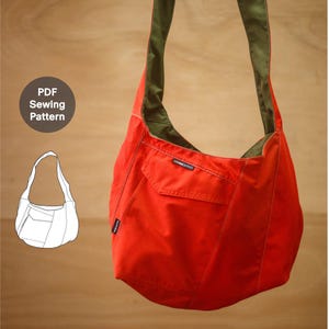 Puede incluir: Un bolso hobo de color naranja brillante con forro y correa de color verde oliva, que presenta un bolsillo frontal con solapa y una pequeña etiqueta negra con la inscripción "STORMEDENCE". Se observa un dibujo lineal blanco del bolso y el texto "PDF Sewing Pattern".