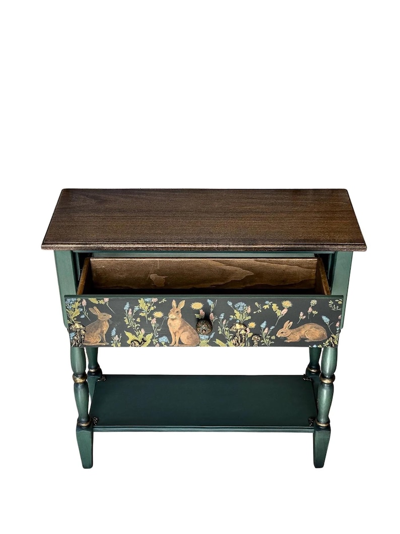 Top view of a hand-painted green console table with an open drawer, showing the woodland rabbit motif on the front panel. The piece features a dark wood top, turned legs, gold accents, and a lower shelf, shown on a white background.
