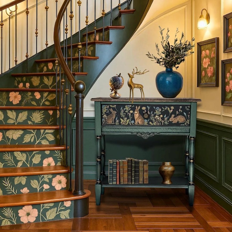 Hand-painted green console table with a woodland rabbit motif, styled in an elegant entryway beside a curved staircase. The table features detailed floral artwork, turned legs, lower shelf with books, and decorative items on top, including a blue vase and brass deer.