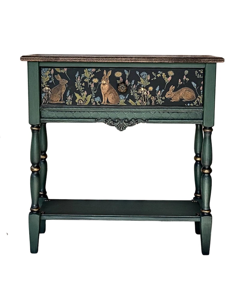 Hand-painted green console table featuring a woodland rabbit design on the front panel, shown isolated on a white background. The piece has turned legs, subtle gold accents, and a lower shelf.
