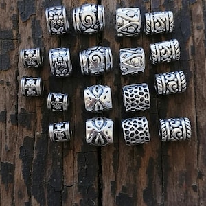 May include: A variety pack of 18 silver beads with large holes, approximately 4-7mm. The beads feature various designs, including floral, swirl, and geometric patterns. The beads are displayed on a weathered wooden surface.