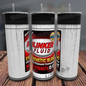 May include: White tumbler with a black lid and a straw. The tumbler has a graphic of a can of "Blinker Fluid" with the text "Up to 10,000 Blinks", "Synthetic Blend", "LED & Filament Compatible", "Max Strength ID-10T", and "Formula".