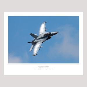 May include: A gray EA-18G Growler jet aircraft in flight against a blue sky. The image includes text at the bottom that reads "UNITED STATES NAVY VAQ-129 "VIKINGS" EA-18G GROWLER DEMONSTRATION TEAM."