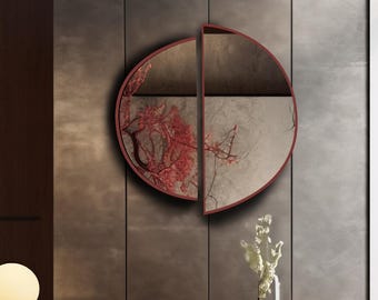 Pode incluir: Um espelho de parede circular dividido em duas metades distintas com uma moldura fina de cor vermelho-escura. O lado esquerdo do espelho apresenta uma superfície refletora com um design de ramo floral vermelho, enquanto o direito é claro.