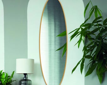 Pode incluir: Um espelho de parede alto e oval com uma moldura fina de cor dourada metálica. O espelho tem uma superfície de vidro lisa e refletora que capta a luz e o espaço circundantes, proporcionando um reflexo vertical claro e alongado.