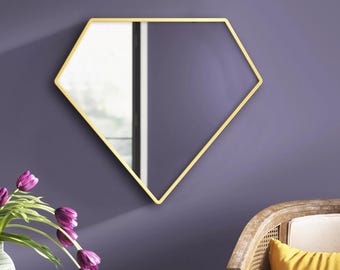 Pode incluir: Um espelho de parede com uma moldura fina de metal dourado em forma de diamante ou pentágono. O espelho apresenta uma superfície de vidro refletora que mostra uma vista parcial de uma janela e espaço interior, montado numa parede roxa.