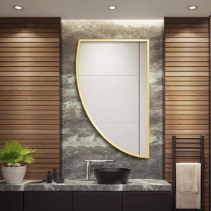 May include: A semi-circular wall mirror featuring a thin gold-toned metal frame. The mirror has a flat vertical edge on the right side and a curved edge on the left side, reflecting a bright interior space with white wall panels and clean lines.