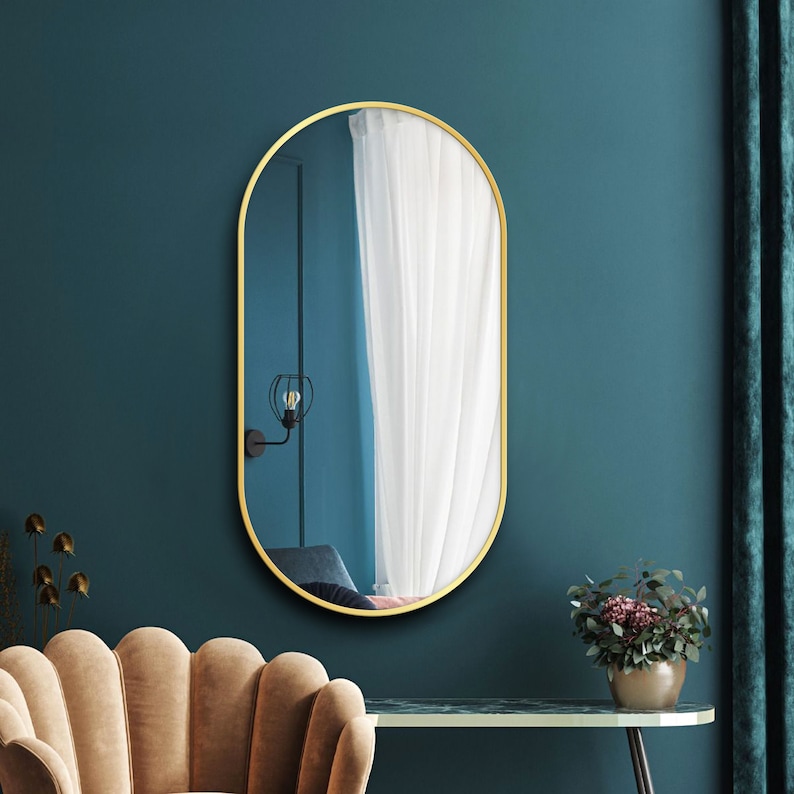 Puede incluir: Un espejo ovalado dorado con una cortina blanca reflejada en el vidrio. El espejo est&aacute; colgado en una pared azul turquesa.