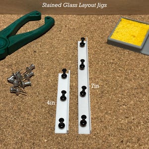 May include: Two white plastic strips with black push pins, labelled 4 in and 7 in. The strips are used for stained glass layout jigs.  There are also a pair of pliers, a small sponge, and a bowl of solder.