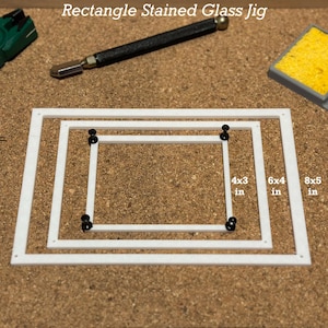 Puede incluir: Un jig de plástico blanco con tres marcos rectangulares de diferentes tamaños para proyectos de vitrales. Los marcos están etiquetados como 4x3 pulgadas, 6x4 pulgadas y 8x5 pulgadas. Hay alfileres negros en cada esquina de los marcos.